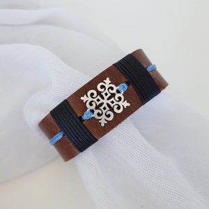 Könnte beinhalten: Ein braunes Lederarmband mit schwarzen und blauen Schnüren und einem silbernen Schneeflocken-Anhänger.
