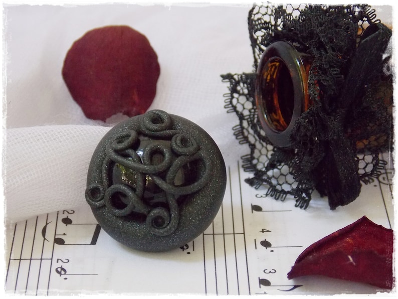 May include: A black and gray decorative bead with a swirling pattern. The bead is on a white surface with musical notes printed on it.