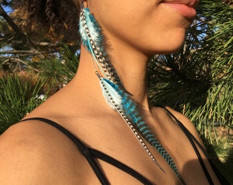 May include: A pair of long, blue and white feather earrings with a silver chain. The feathers are layered and have a black and white pattern.
