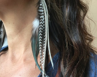 May include: A pair of long feather earrings with white, black, and brown feathers. The earrings are hanging from a person's ear.