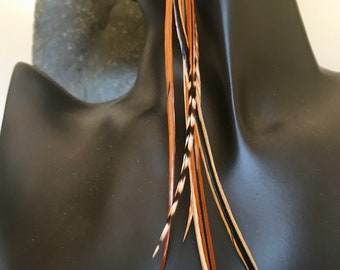 May include: A set of brown, black, and white feathers with a long, flowing design. The feathers are attached to a string and are likely used for hair extensions or as a decorative element.