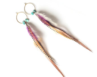 May include: A pair of gold hoop earrings with turquoise beads and long, colorful feathers. The feathers feature shades of purple, white, brown, and black, creating a bohemian style.
