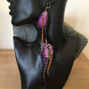 May include: Long purple and brown feather earrings with a silver hook. The feathers are layered and have a delicate, bohemian style.