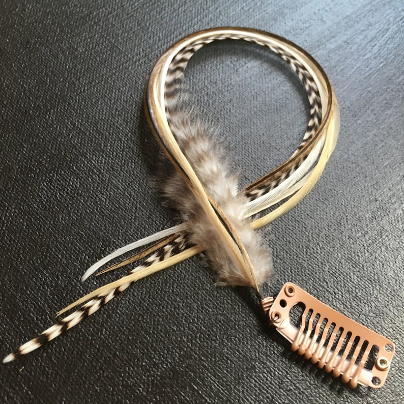 May include: A set of brown, white, and black feathers with a copper-colored hair clip. The feathers are tied together and have a natural, rustic look.