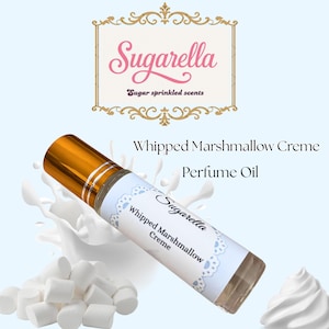 Peut inclure: Un flacon de parfum à bille avec un bouchon doré et une étiquette indiquant "Sugarella Whipped Marshmallow Creme". L'image comprend des guimauves, de la crème fouettée et le texte "Sugar sprinkled scents".