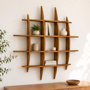 Könnte beinhalten: Ein hölzernes Wandregal mit Gitterdesign, das dekorative Gegenstände enthält. Das Regal besteht aus hellbraunem Holz und verfügt über mehrere horizontale Regale und vertikale Stützen. Zu den Gegenständen auf den Regalen gehören eine Topfpflanze, Bücher, eine Vase und eine Kerze.