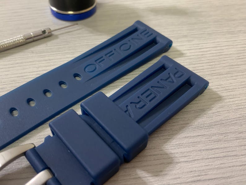 May include: Close-up of a navy blue watch strap with the brand name "OFFICINE PANERAI" embossed on the rubber. A small screwdriver and a watch component are visible in the background.