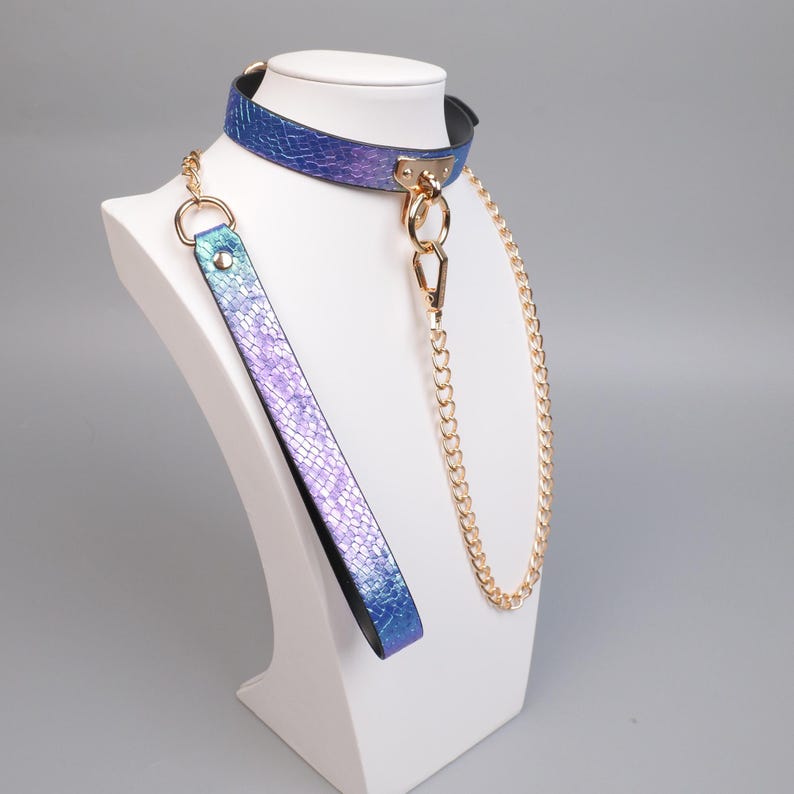 May include: A blue and purple iridescent collar and leash set. The collar is displayed on a white mannequin head. The set includes a gold chain and hardware. The leash is a matching iridescent material.