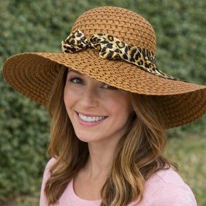 Puede incluir: Sombrero de paja de ala ancha, tejido, en tonos marrón y beige. Cuenta con una cinta con estampado de leopardo atada con un lazo. El sombrero está diseñado para la protección solar y la moda.