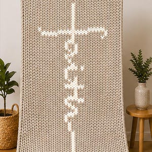 May include: A beige knitted throw blanket with the word "Faith" in white, vertically aligned, and a white cross at the top. The blanket has a thick, textured knit pattern and a rope-like border.