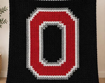 May include: A black knitted blanket with a large red and white letter "O" in the center. The blanket has red and white stripes at the top and bottom edges. The blanket is held up by a person.