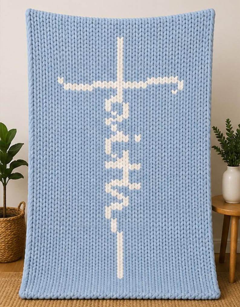 May include: A light blue knitted blanket with the word "Faith" in white, vertically centered, and a white cross at the top. The blanket is made of thick, chunky knit yarn. The blanket is displayed on a light background.
