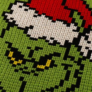 May include: Close-up of a green, red, white, black, and yellow pixelated design. The design features a character's face with a red hat, white face, black eyes, and a green background.