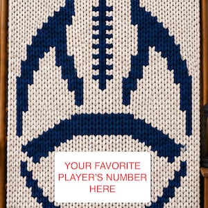 May include: A chunky knit blanket in cream with a large dark blue football graphic. The design features a central vertical stitch pattern and a white rectangular overlay with the red text: YOUR FAVORITE PLAYER’S NUMBER HERE.