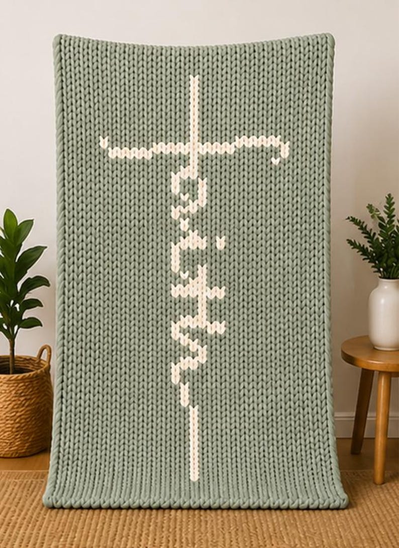 May include: A sage green knitted blanket with the word "Faith" in white, vertically centered. The word is designed with a cross at the top. The blanket is displayed indoors.