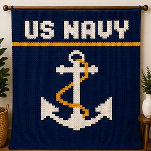 May include: A dark blue knitted wall hanging featuring the white text US NAVY at the top, a horizontal yellow stripe, and a large white anchor graphic with a yellow rope detail in the center, all suspended from a wooden rod.