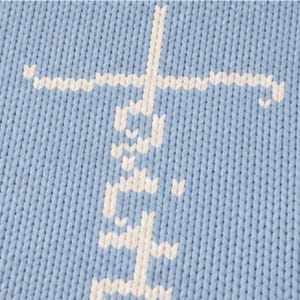May include: Close-up of a light blue knitted fabric with a white cross design. The cross is made of a series of small, connected stitches, creating a textured appearance. The fabric has a visible knit pattern.