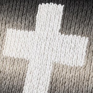 May include: A white cross design is prominently displayed against a backdrop of varying shades of gray and beige. The cross appears to be made of a thick, textured material, creating a tactile appearance. The background has a gradient effect.