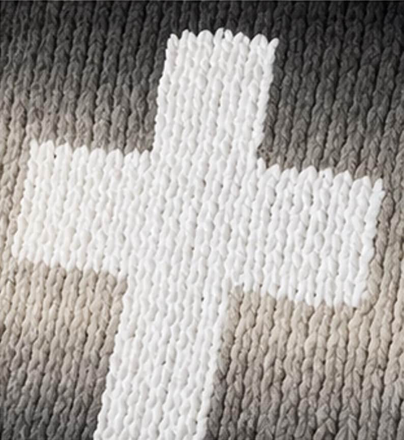May include: A white cross design is prominently displayed against a backdrop of varying shades of gray and beige. The cross appears to be made of a thick, textured material, creating a tactile appearance. The background has a gradient effect.