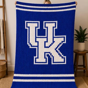 May include: A blue knitted blanket with a large white "UK" logo. The blanket has white stripes at the top and bottom. The blanket is made of a thick, textured material, perfect for keeping warm.