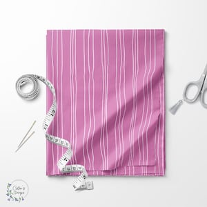 Puede incluir: Una tela rosa doblada con líneas blancas verticales, una cinta métrica, agujas y tijeras. La tela tiene un patrón de finas líneas blancas onduladas sobre un fondo rosa liso. La cinta métrica es blanca con marcas negras. Las tijeras son plateadas.