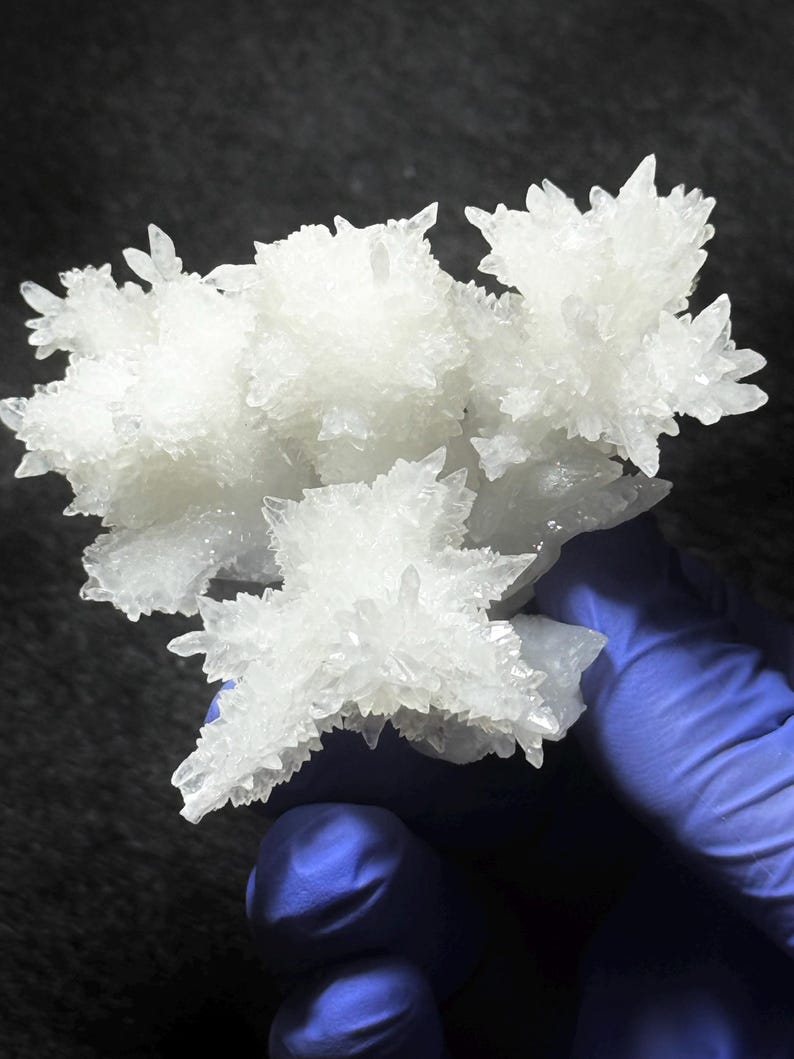 Puede incluir: Un racimo de cristales blancos transl&uacute;cidos con bordes afilados y puntiagudos y una estructura dentada y ramificada. La formaci&oacute;n mineral presenta m&uacute;ltiples puntas radiantes que crean una apariencia compleja y multifac&eacute;tica con una superficie brillante.