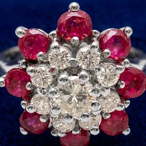 May include: A silver-toned ring featuring a central round white diamond surrounded by a cluster of smaller white diamonds, encircled by an outer layer of eight vibrant round-cut red rubies set in a floral-inspired arrangement on a metal band.