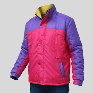 May include: A colour-blocked puffer jacket featuring a bright pink main body, purple sleeves and upper chest panels, and a yellow inner collar. The jacket includes a front button closure, two chest pockets, and two lower side pockets with purple trim.