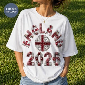 Może przedstawiać: Biała koszulka z napisem "ENGLAND" i rokiem "2026" w czerwono-białym wzorze. Projekt zawiera piłkę nożną z krzyżem i tekst "3 DESIGNS INCLUDED" w niebieskim okręgu.