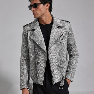 May include: A gray and white snakeskin-patterned leather jacket with a black zipper closure and belt. The jacket has a notched collar and a classic biker style. The person is wearing black sunglasses and a black t-shirt.