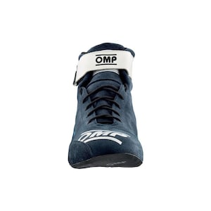 May include: A navy blue suede racing boot with a white strap and the text "OMP". The boot has black laces and a white logo on the side. The sole is black.