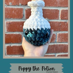 May include: A plush crochet potion bottle featuring a white top section and a dark blue, teal, and black mottled bottom section. The bottle has two large black safety eyes and a small tan cork-like topper. Text below reads: Poppy the Potion Crochet Pattern Created by TerraFibers.