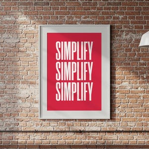 Puede incluir: Un cartel enmarcado con la palabra "SIMPLIFICAR" repetida tres veces en blanco sobre un fondo rojo. El cartel está montado en una pared de ladrillo.