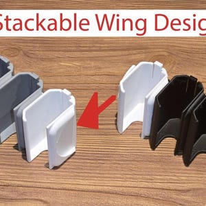 Puede incluir: La imagen muestra varios componentes de diseño de ala apilables en gris, blanco y negro. El texto "Stackable Wing Design!" se muestra en un rectángulo blanco con borde rojo. Los componentes están dispuestos sobre una superficie de madera.