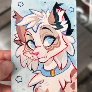 Puede incluir: Ilustración en acuarela de la cara de un gato sobre una tarjeta rectangular. El gato tiene ojos azules, nariz rosa y un collar azul claro con una etiqueta dorada. El pelaje del gato es blanco, marrón y negro, con fondo azul claro y detalles de estrellas.