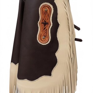 May include: Leather chaps in brown and cream, with floral tooling and fringe. The chaps have a dark brown front panel, cream side panels, and decorative accents. The chaps are designed for riding.
