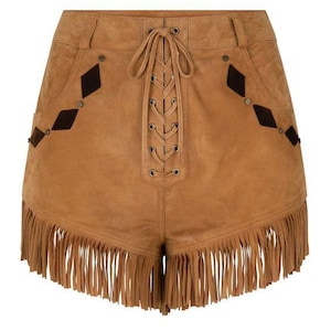 May include: Tan suede shorts with a lace-up front and fringing. The shorts have diamond-shaped details and pockets. A stylish, bohemian-inspired garment.