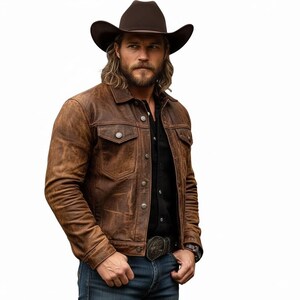 May include: A brown leather jacket with two chest pockets and button closures. The jacket is worn over a black shirt and blue jeans. A brown cowboy hat and belt buckle complete the western look.