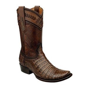 Könnte beinhalten: Brauner Leder-Cowboy-Stiefel mit spitzer Zehenpartie. Der Stiefel hat ein strukturiertes Krokodilmuster auf dem Fuß und ein dekoratives Nahtdesign am Schaft. Der obere Teil des Stiefels hat eine dunklere braune Farbe.