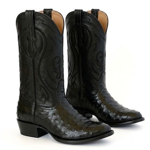 Peut inclure: Une paire de bottes de cowboy noires avec un motif texturé sur le pied et une tige en cuir lisse ornée de surpiqûres ton sur ton. Les bottes présentent un bout pointu, un talon bottier et une doublure intérieure beige visible à l'ouverture.