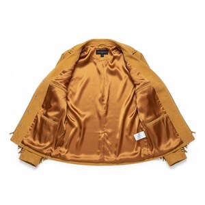 May include: Open view of a tan suede jacket with fringe detailing along the sleeves and hem. The jacket has a satin-like gold interior lining and two front pockets. The jacket is buttoned and has a classic collar.