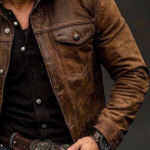 May include: A brown leather jacket with a button-down front and two chest pockets. The jacket has a distressed appearance and is worn over a black shirt. The image shows a close-up of the jacket's details, including the buttons and stitching.