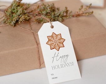 Può includere: Un'etichetta regalo bianca con un disegno di biscotto di pan di zenzero marrone e la scritta "Happy Holidays!" in corsivo nero. L'etichetta è legata con spago a un pacco avvolto. Il verde aggiunge un tocco naturale.