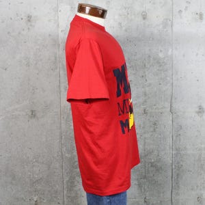 May include: A red t-shirt with the word "Mickey" in navy blue block letters and a yellow cartoon character. The shirt is made of a soft material and has short sleeves.