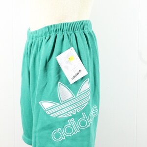 May include: Teal athletic shorts with a white Adidas logo and the word "adidas" printed on the leg. The shorts have an elastic waistband.