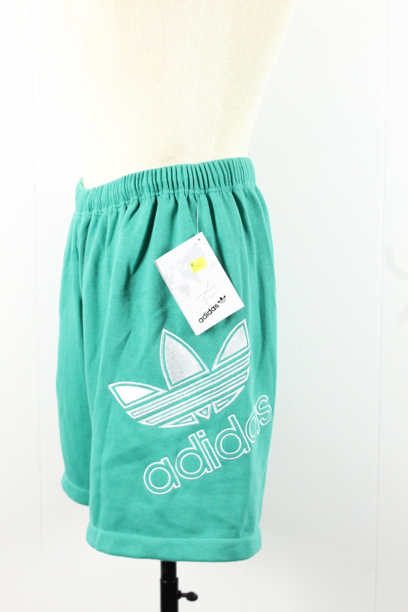 May include: Teal athletic shorts with a white Adidas logo and the word "adidas" printed on the leg. The shorts have an elastic waistband.