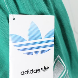 May include: A green Adidas sweatshirt with a white Adidas logo and a white tag that says "adidas" with a blue and white Adidas logo.