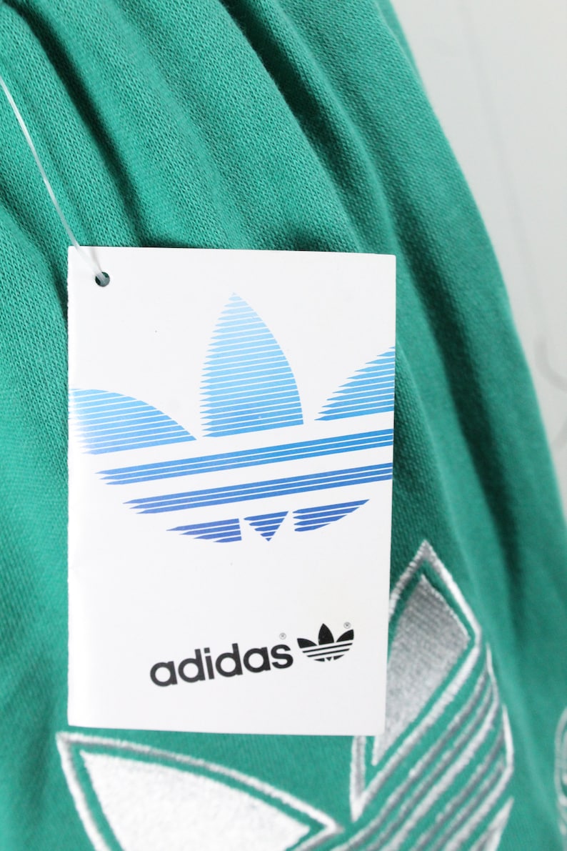 May include: A green Adidas sweatshirt with a white Adidas logo and a white tag that says "adidas" with a blue and white Adidas logo.