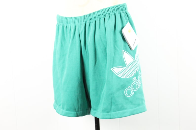 May include: Teal athletic shorts with a white Adidas logo on the right leg. The shorts have an elastic waistband and a drawstring.