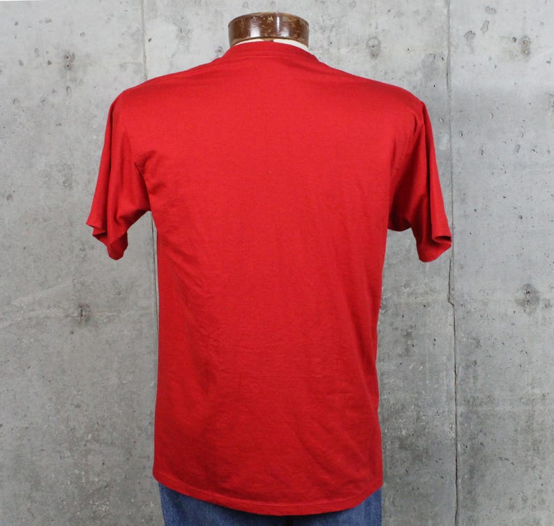 May include: A solid red t-shirt with short sleeves, displayed on a mannequin. The shirt is made of a soft material and has a classic crew neck. The back of the shirt is visible, showing the simple design.